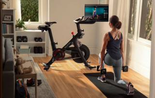 Peloton bike with woman working out with dumbbells in a squat with screen rotated to face her.